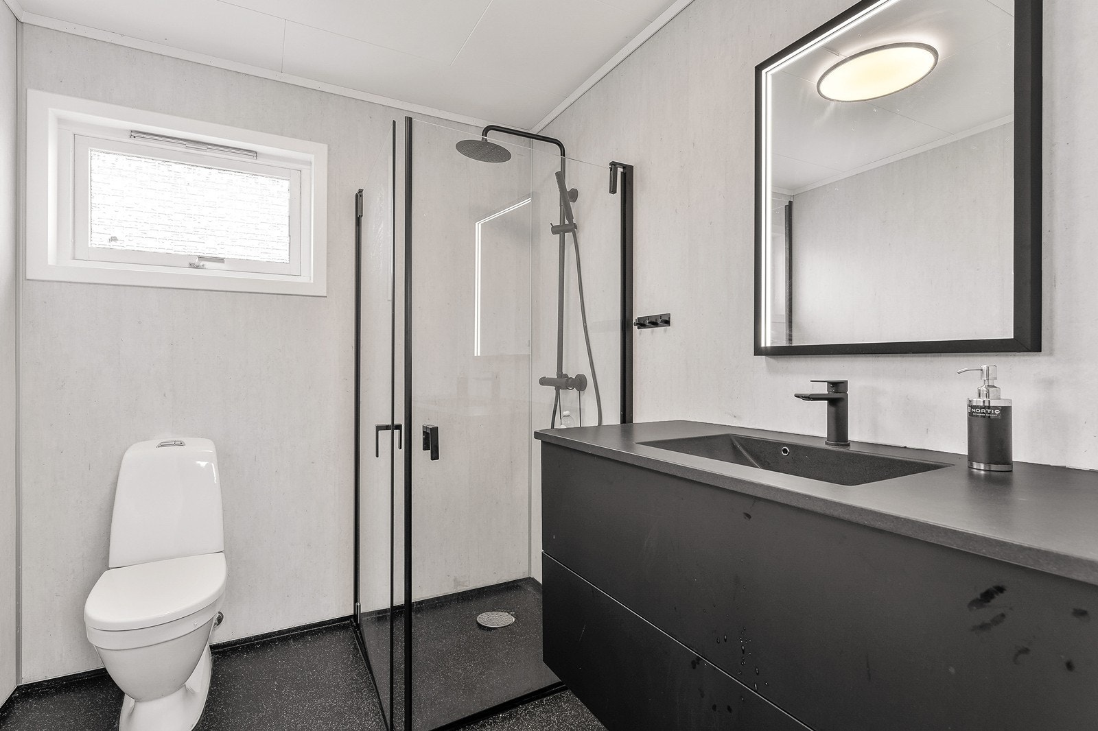 Bad med baderomsplater på vegg og belegg og varmekabler i gulv. Innredet med toalett, dusjhjørne med glassdører og romslig servantskap og speil. Galleribilde