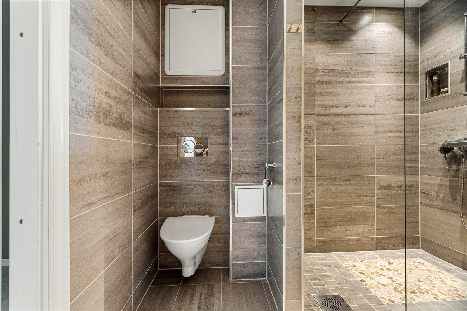 Badet er innredet med vegghengt toalett, benkeskap med servant, skapinnredning og dusjvegg i glass. Badet har opplegg for vaskemaskin, samt at fordelerskap til rør-i-rør vannforsyning er plassert her. Galleribilde