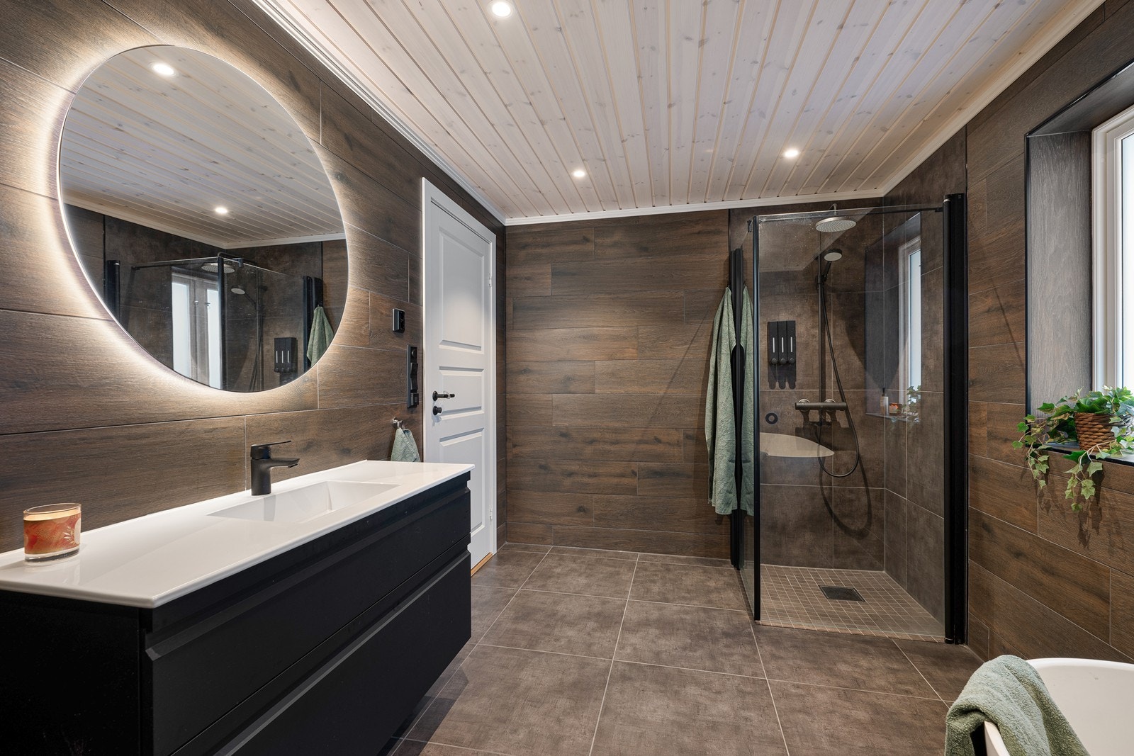 Badet er innredet med servant i baderomsinnredning med speil over, dusjhjørne med glassvegger, et moderne badekar og vegghengt toalett. Galleribilde