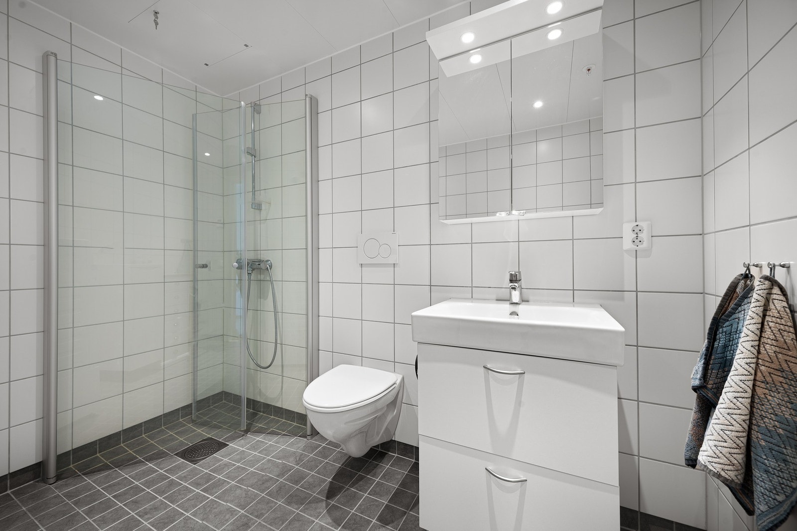 Badet inneholder dusjnisje med praktiske innfellbare glassdører - det er også opplegg for vaskemaskin Galleribilde