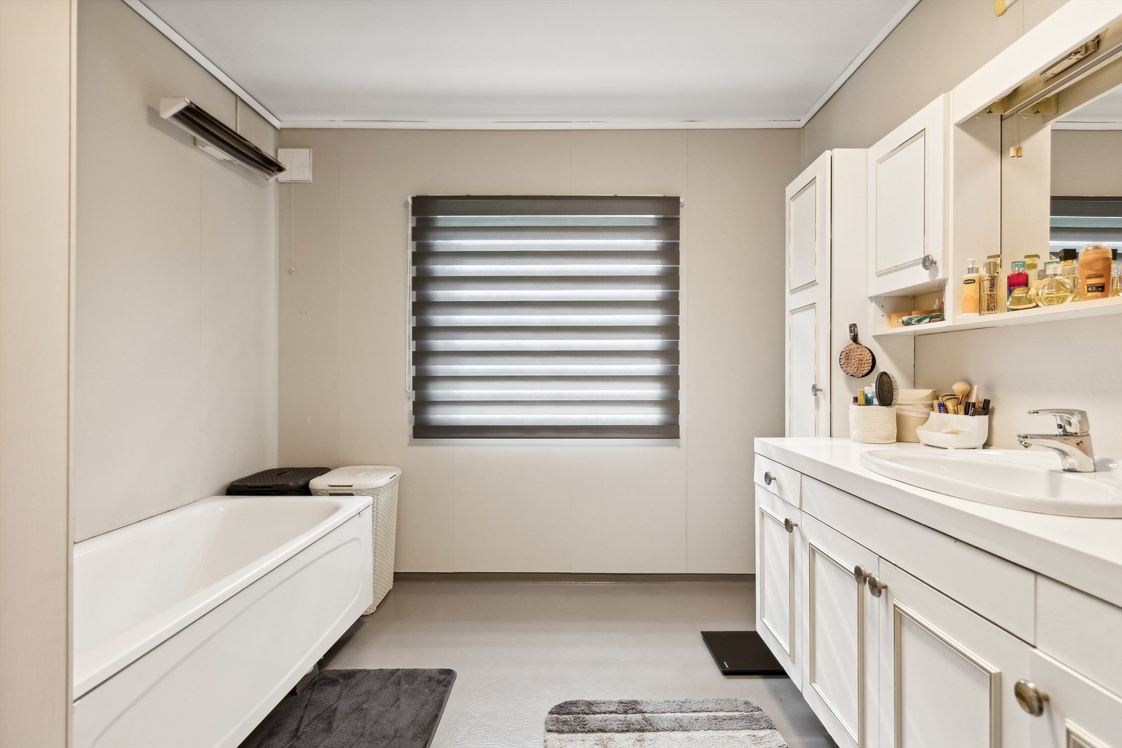 Lyst baderom med badekar og baderomsseksjon med servant og speil. Galleribilde