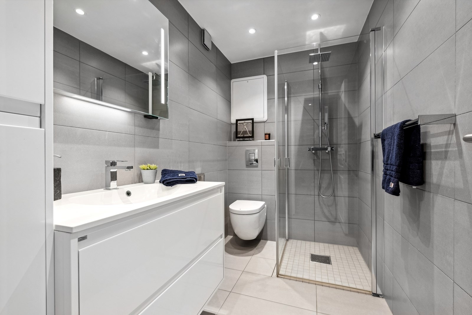 Delikat baderom innredet med dusjhjørne, servant med overskap og vegghengt toalett. Galleribilde