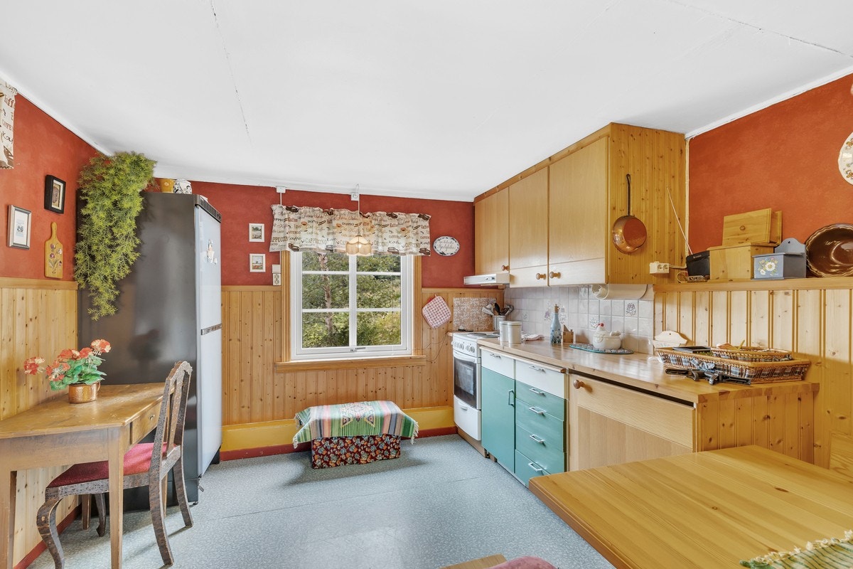 Kjøkkenet er innredet med glatte og profilerte fronter, frittstående komfyr, vaskemaskin og kjøleskap. Galleribilde