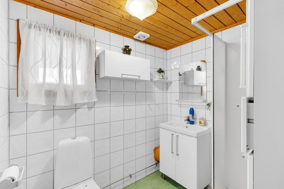 Baderom med flislagt gulv med gulvvarme, innredet med toalett, dusj og servantinnredning med speil. Galleribilde