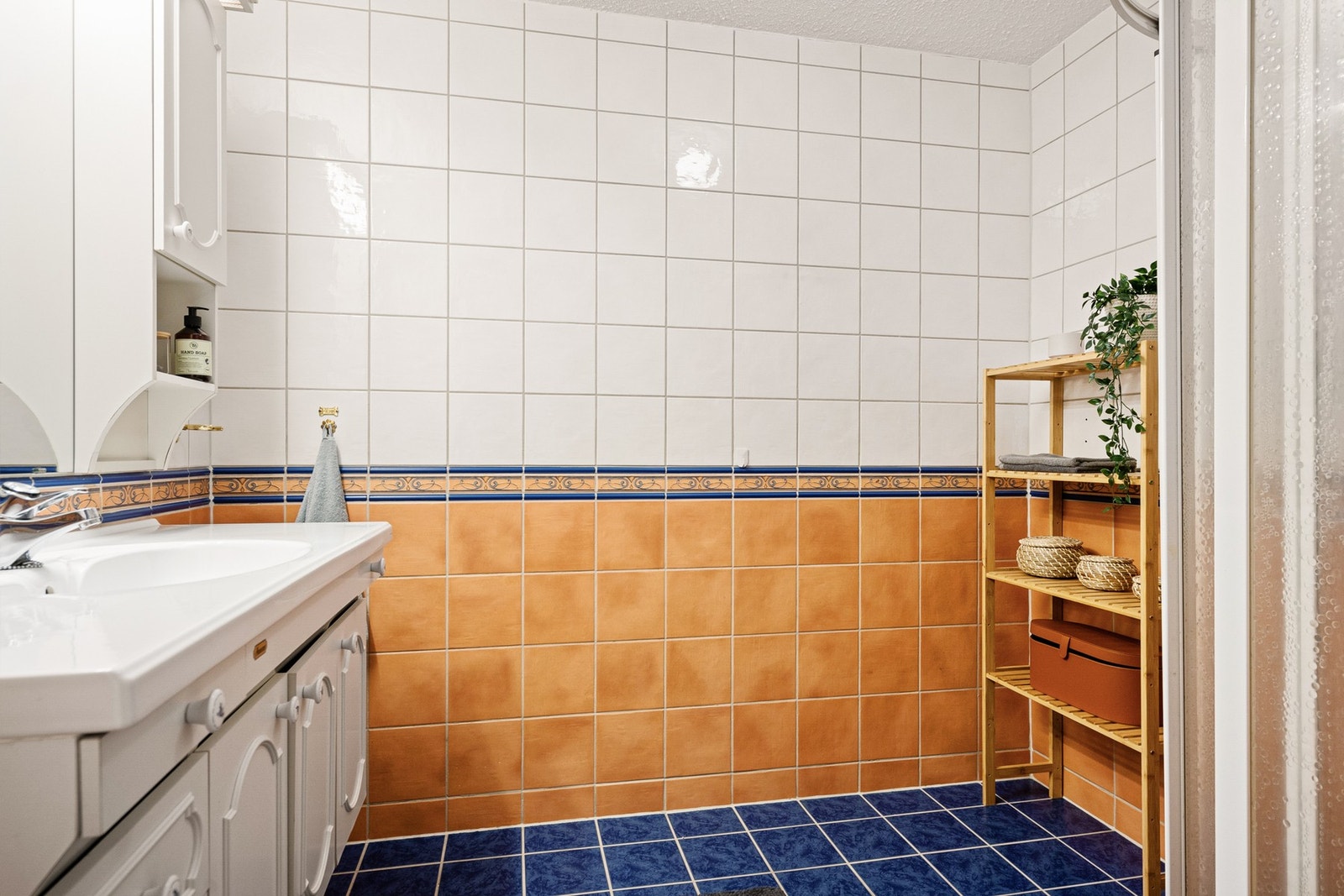 Det flislagte badet har servant med innredning og dusjkabinett Galleribilde