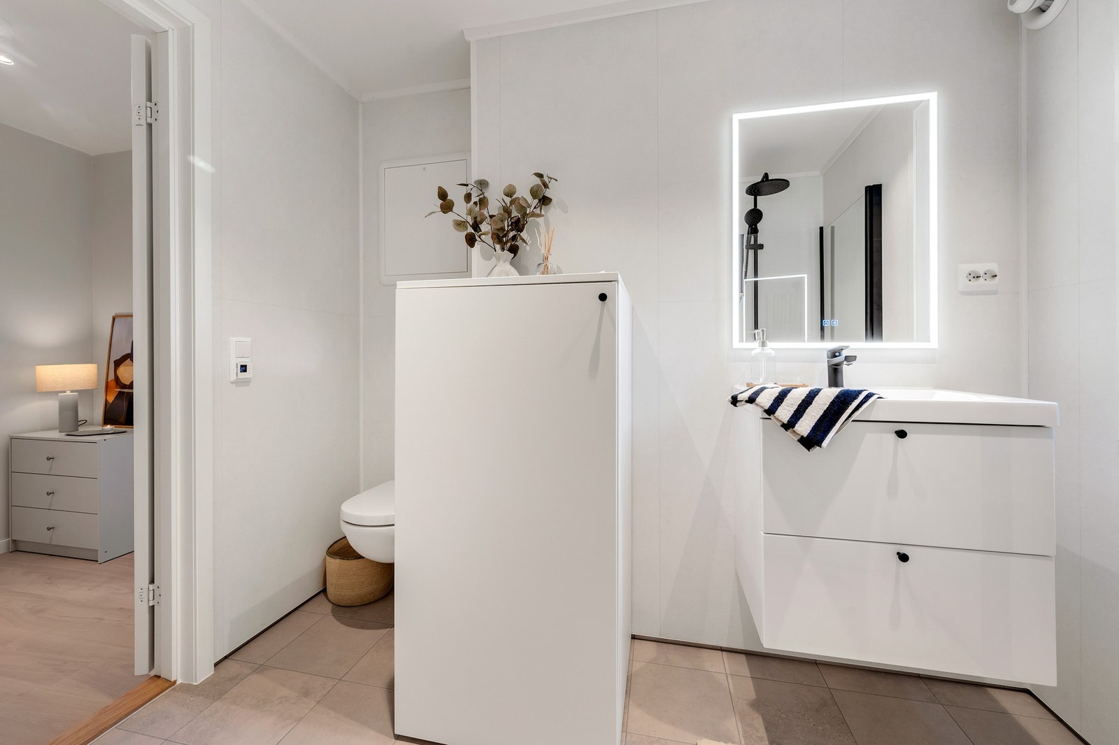 Badet har flis på gulv og er innredet med dusjhjørne, veggmontert WC og servant med underskap. Galleribilde