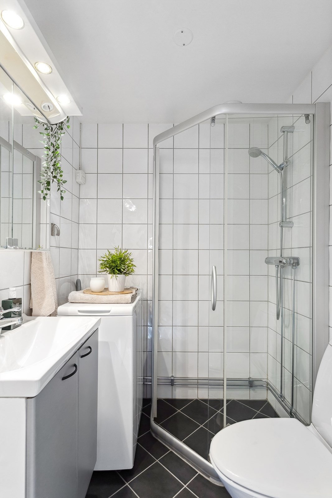 Lyst bad med heldekkende servant på underskap med folierte fronter, speilskap, lysarmatur og gulvmontert klosett Galleribilde