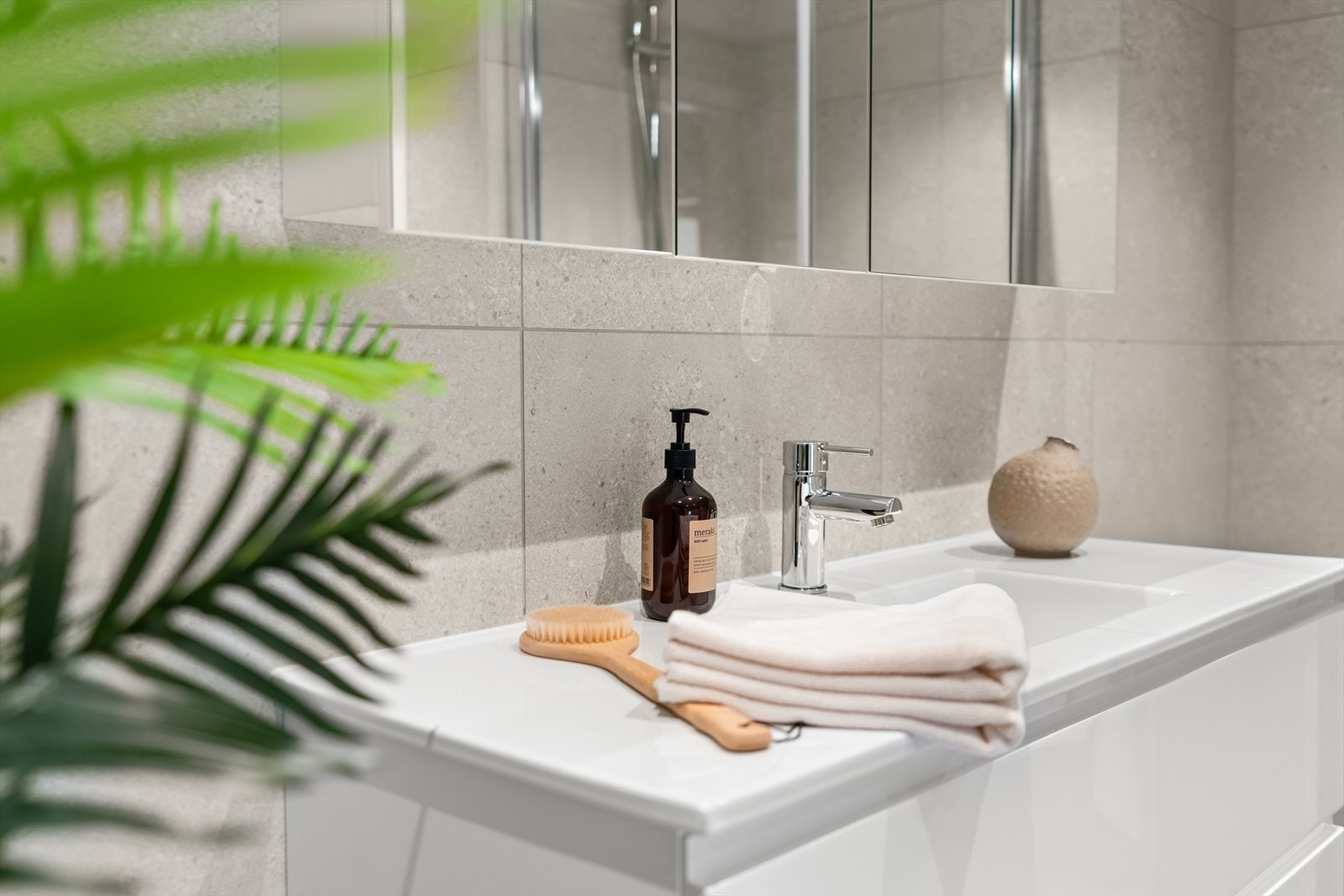 Badet er bygget opp med vegghengt innredning med servant, speilskap, vegghengt toalett, dusjhjørne med innfellbare glassdører og opplegg for vaskemaskin. Galleribilde