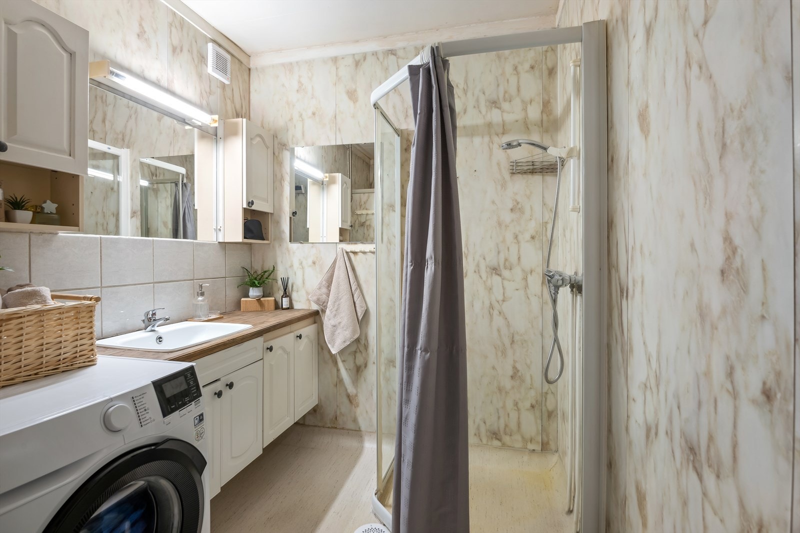 Enkelt bad med baderomsplater på veggene og vinyl på gulvet. Rommet har innredning med nedfelt servant, dusjhjørne og opplegg for vaskemaskin samt mekanisk avtrekk. Trapp inne på baderom belagt med keramiske fliser. Galleribilde