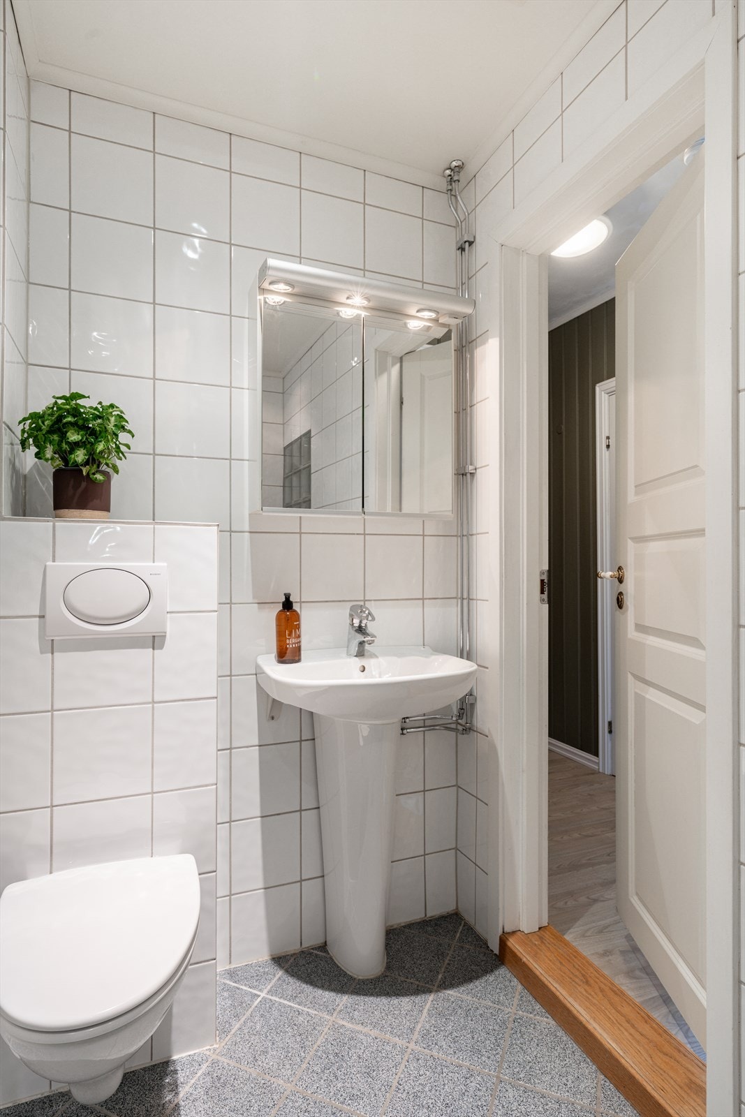 Badet er flislagt og utstyrt med en dusjnisje med dusjdør, en heldekkende servant med ett-greps blandebatteri, og et vegghengt toalett. Galleribilde