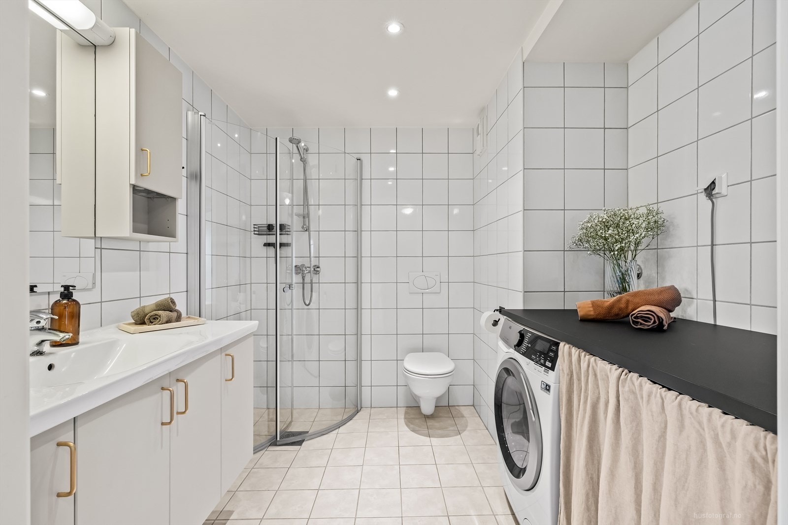 Romslig bad med lys skapinnredning, servant, veggmontert toalett og dusjhjørne. (Benk over vaskemaskin medfølger ikke) Galleribilde