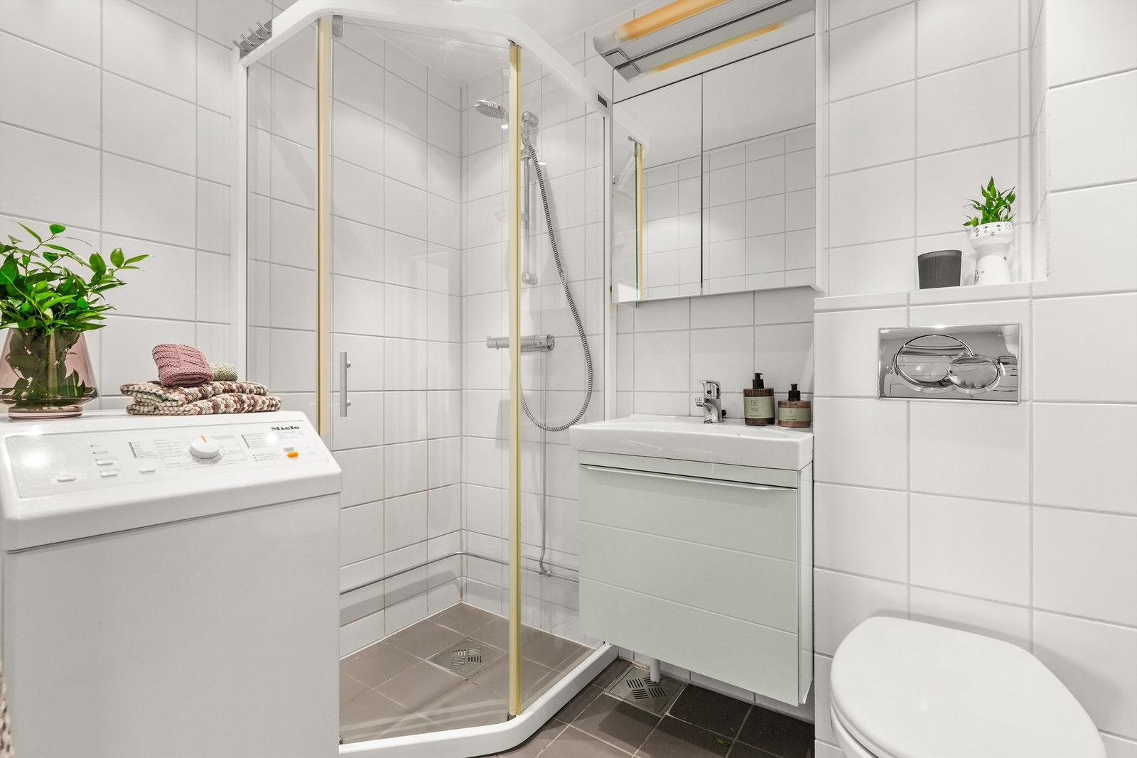 Badet er pent flislagt på gulv og vegger med varme i gulvet. Innredningen består av servant med innredning og med et praktisk speilskap med lys over servanten. Galleribilde