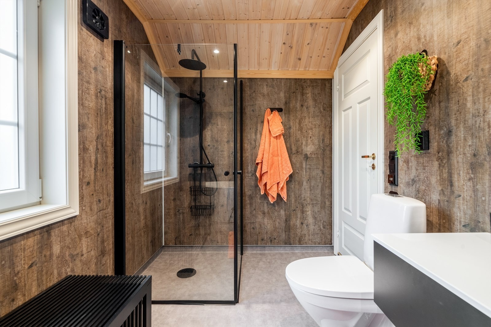 Baderommet utstyrt med gulvmontert toalett, badekar, elektrisk styrt vifte, glassdører til dusjnisje samt dusjgarnityr. Galleribilde