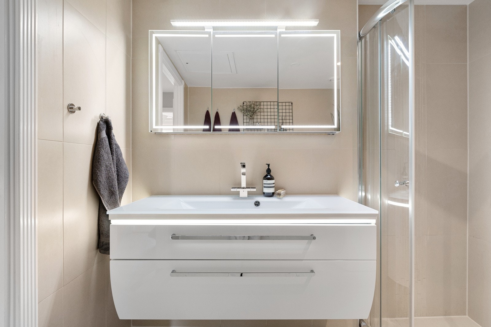 Innredningen består av vegghengt toalett, servant med underskap, overskap med speilfronter og lys, og dusjhjørne med skyvedør. Galleribilde