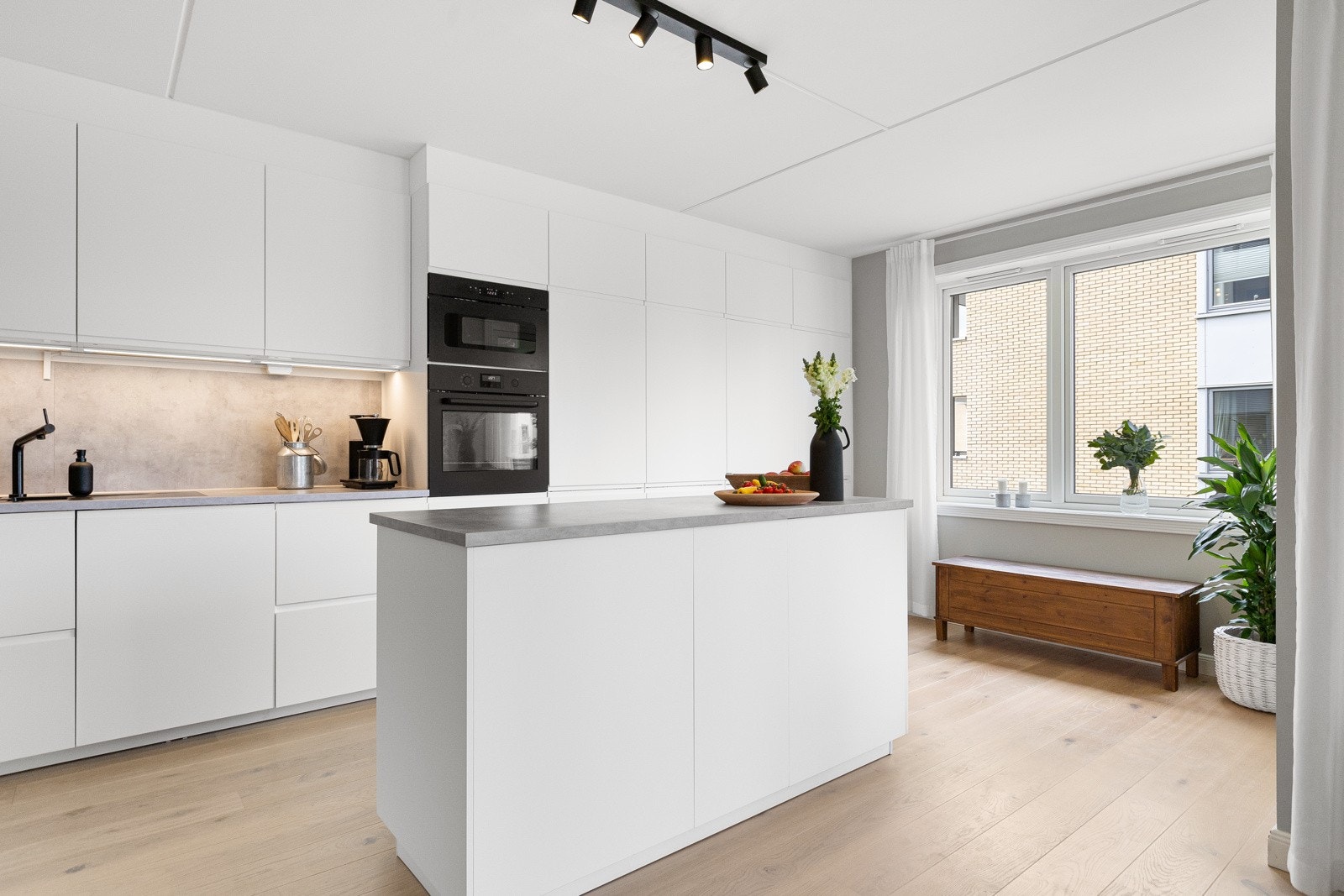 Moderne kjøkken fra 2020 med hvite, slette fronter med innebygde håndtak og stilren laminatbenkeplate med oppvaskkum og sprutplate. Galleribilde