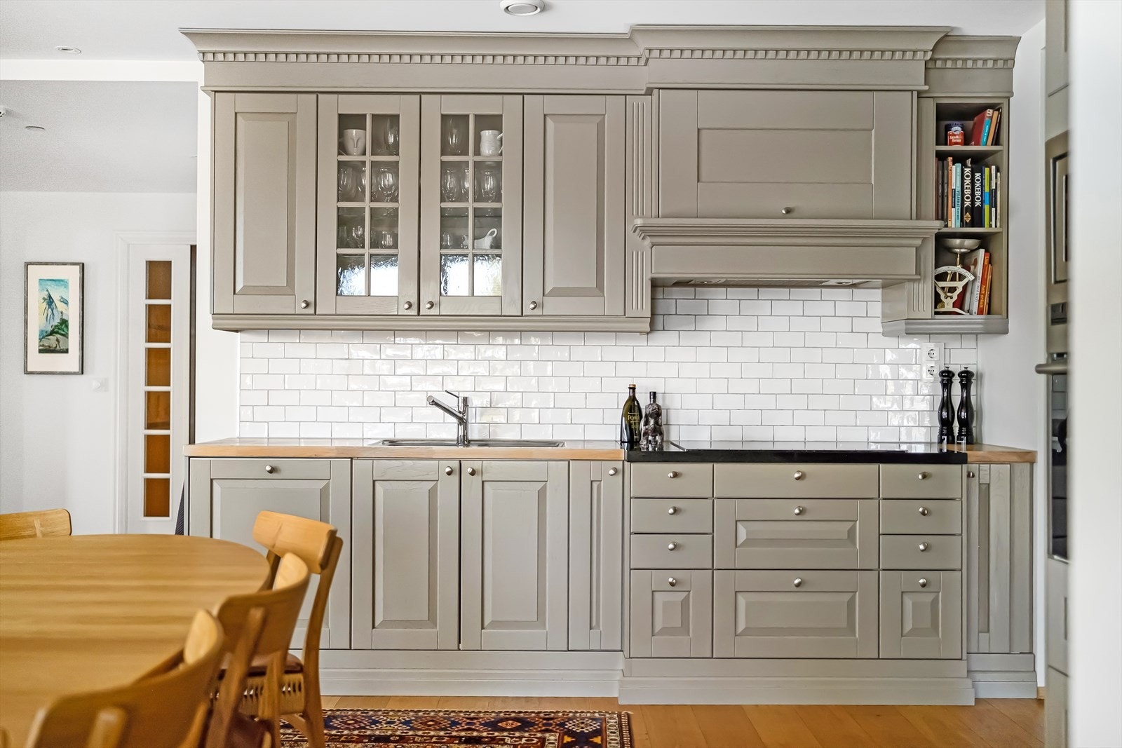 Påkostet og moderne kjøkkeninnredning med stavlimt benkeplater av heltre, flislagt backsplash, avtrekksvifte med kullfilter samt sort granittplate rundt steketoppen. Nedfelt dobbel vaskekum av metall med blandebatteri. Galleribilde