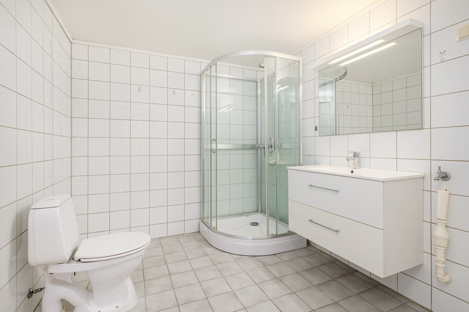 Flislagt baderom med wc, dusjkabinett, servant med praktiske skuffer og opplegg for vaskemaskin Galleribilde