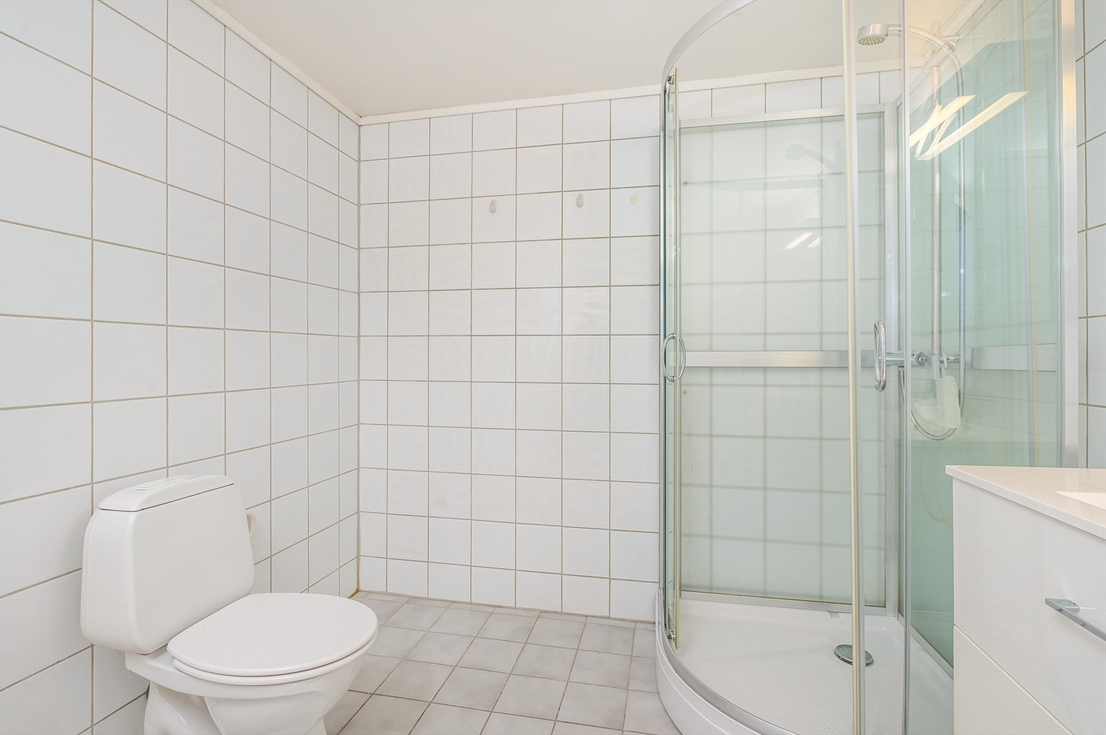 Flislagt baderom med wc, dusjkabinett og opplegg for vaskemaskin Galleribilde