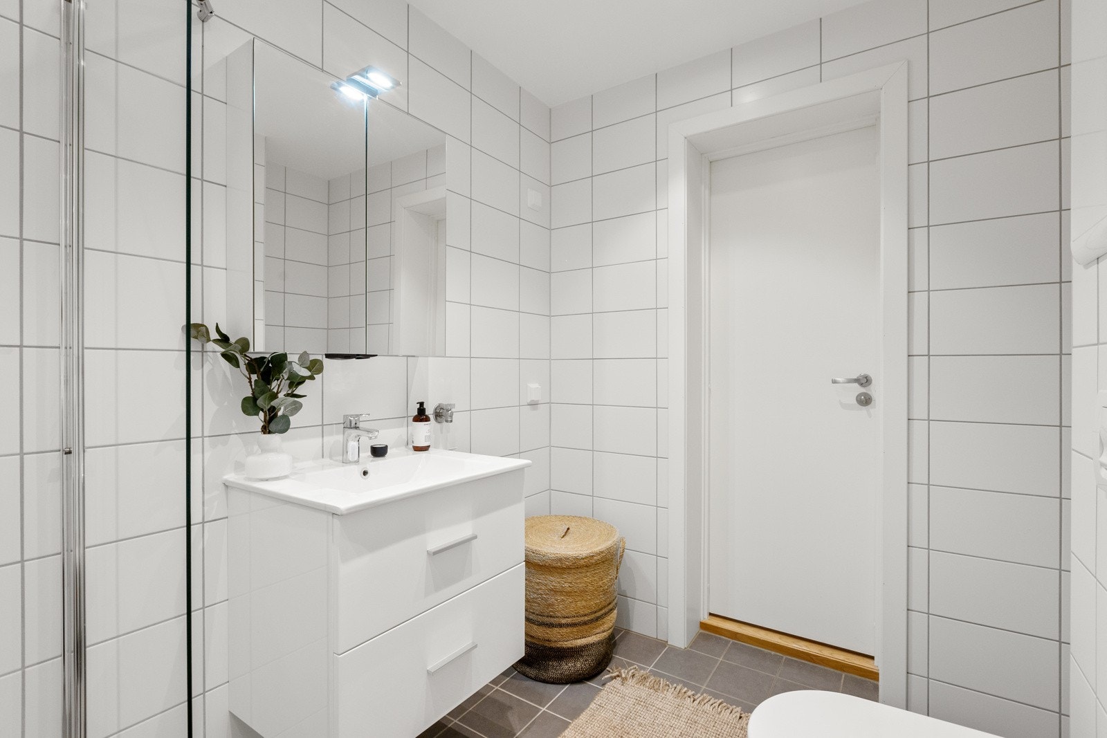 Badet er utstyrt med downlights, vegghengt toalett, servant med underskap, overskap med speilfronter og overlys, og dusj. Det er også opplegg for vaskemaskin. Galleribilde