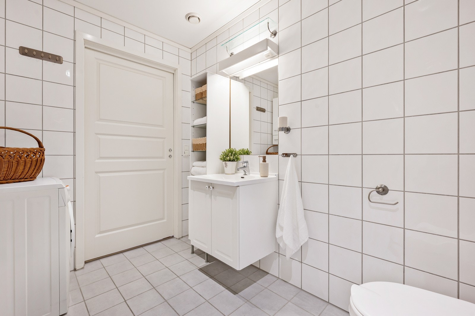 Badet har fliser på vegger og gulv, og gulvet har behagelig gulvvarme. Romslig innredning med skap og hylleløsning. Det er opplegg for vaskemaskin. Galleribilde