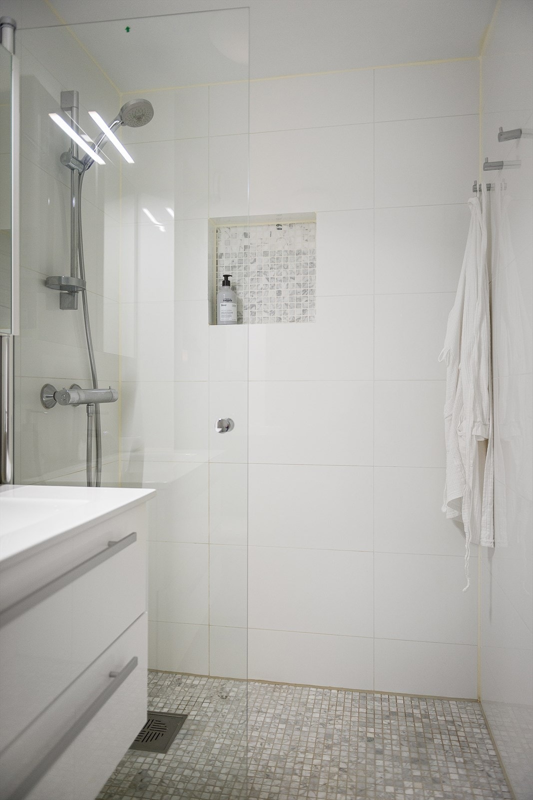 Dusj på gulv med dør i herdet glass og flislagt hylle. Galleribilde