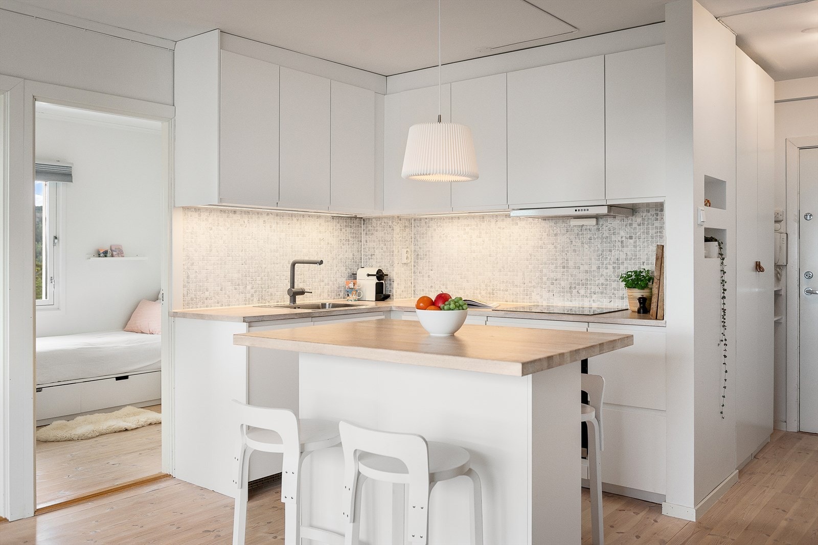 Kjøkkeninnredning med glatte fronter, mosaikkfliser over benkeskap, belysning under overskap og heltre benkeplate. Galleribilde