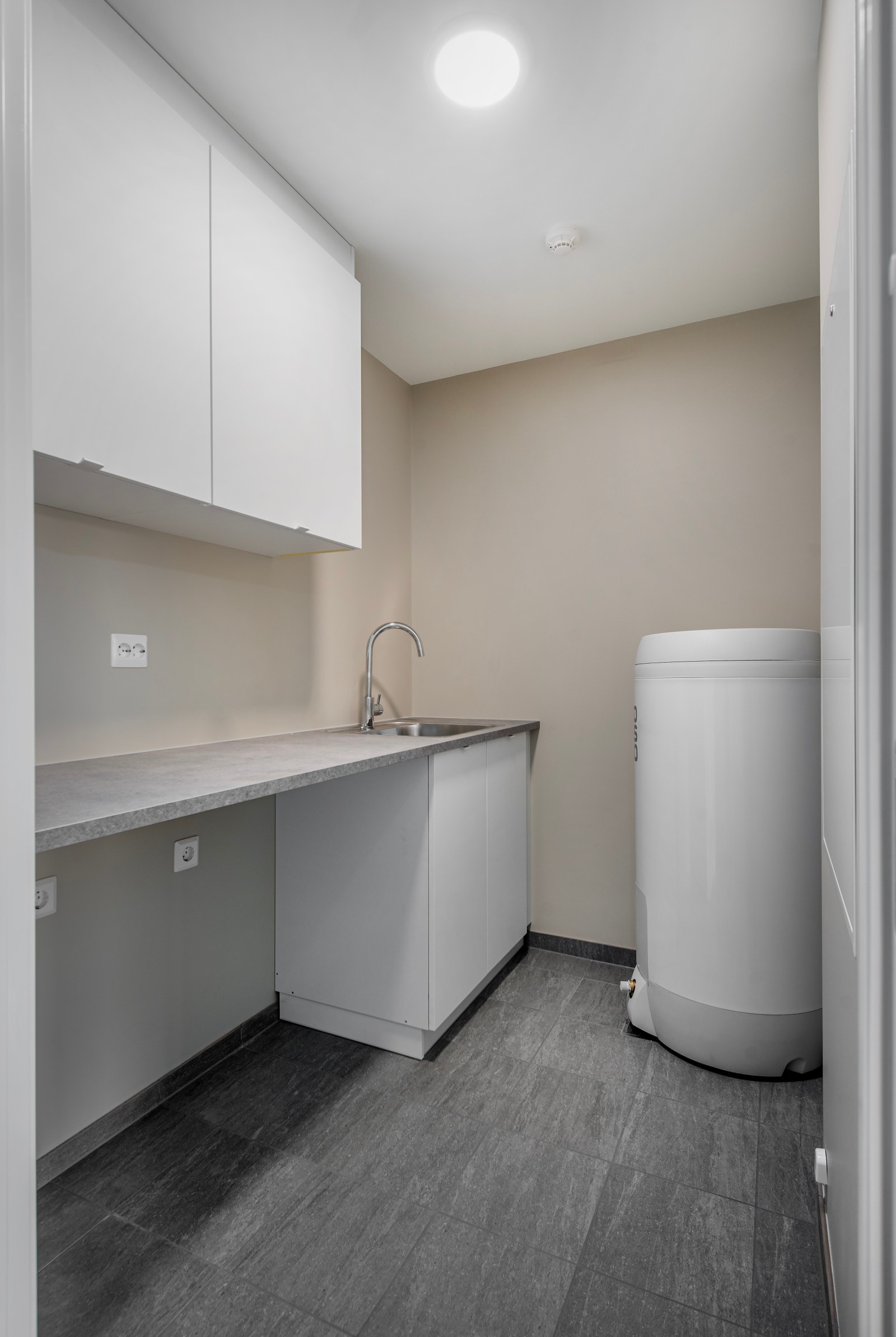 Vaskerommet har praktisk og fin innreiing med overskap, benkeplate og vask. Flis på golv, og på veggane er det malte flater. Opplegg for vaskemaskin og tørketrommel. Galleribilde