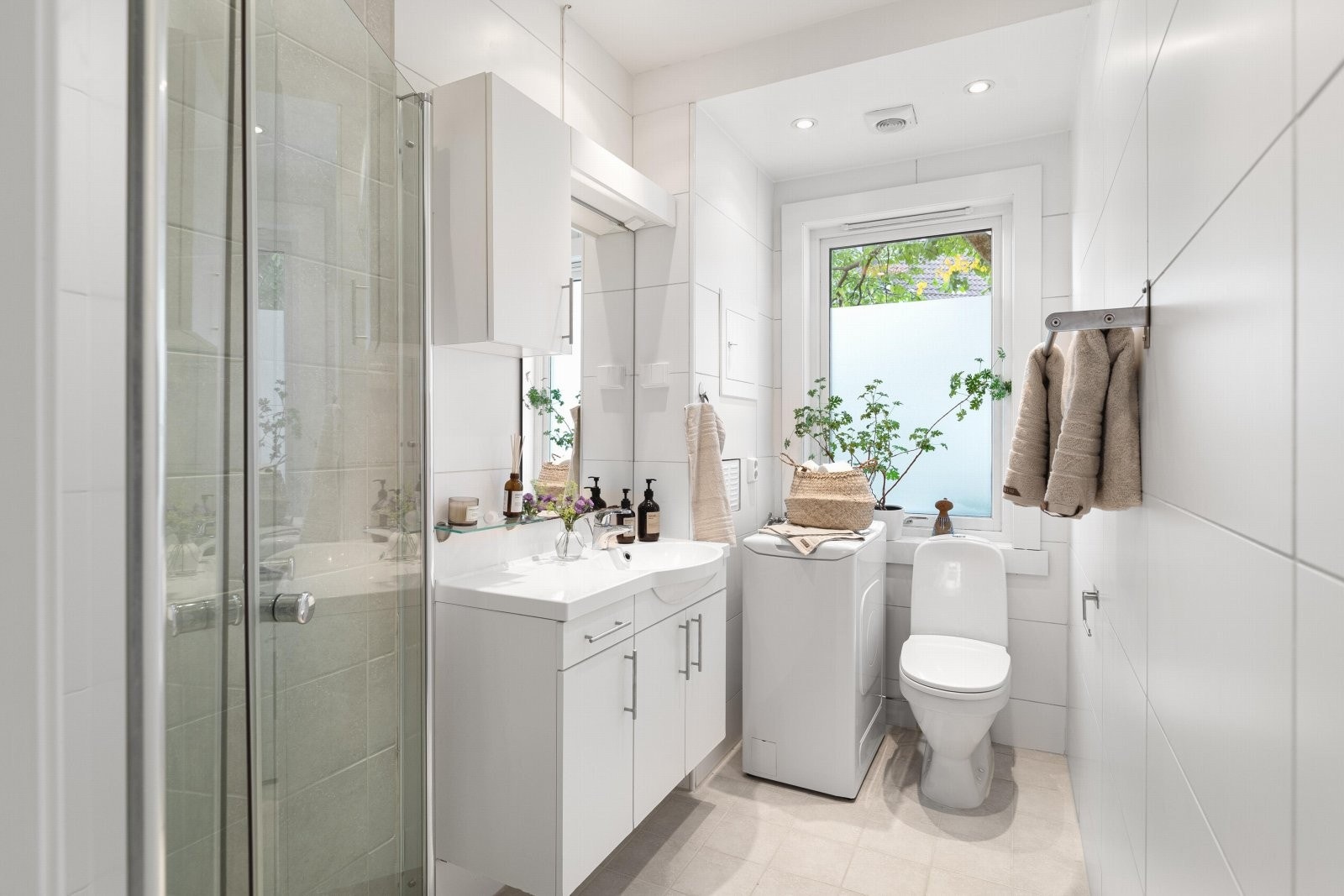 Lyst og flislagt baderom i praktisk utførelse med dusjnisje og opplegg for vaskemaskin Galleribilde