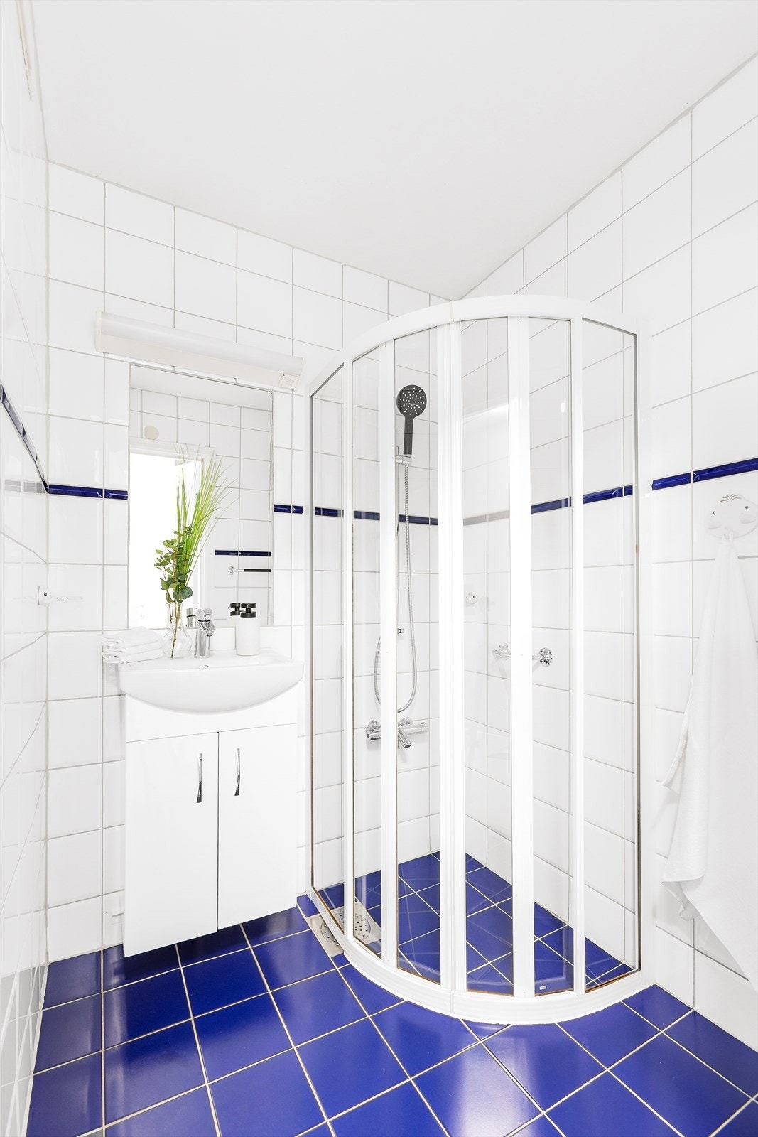 Badet har flislagt gulv med elektriske varmekabler, flislagte vegger, og et malt innvendig tak. Innredningen inkluderer en servant med underskap, et innmurt speil med belysning over, og et dusjhjørne med skyvedører. Galleribilde