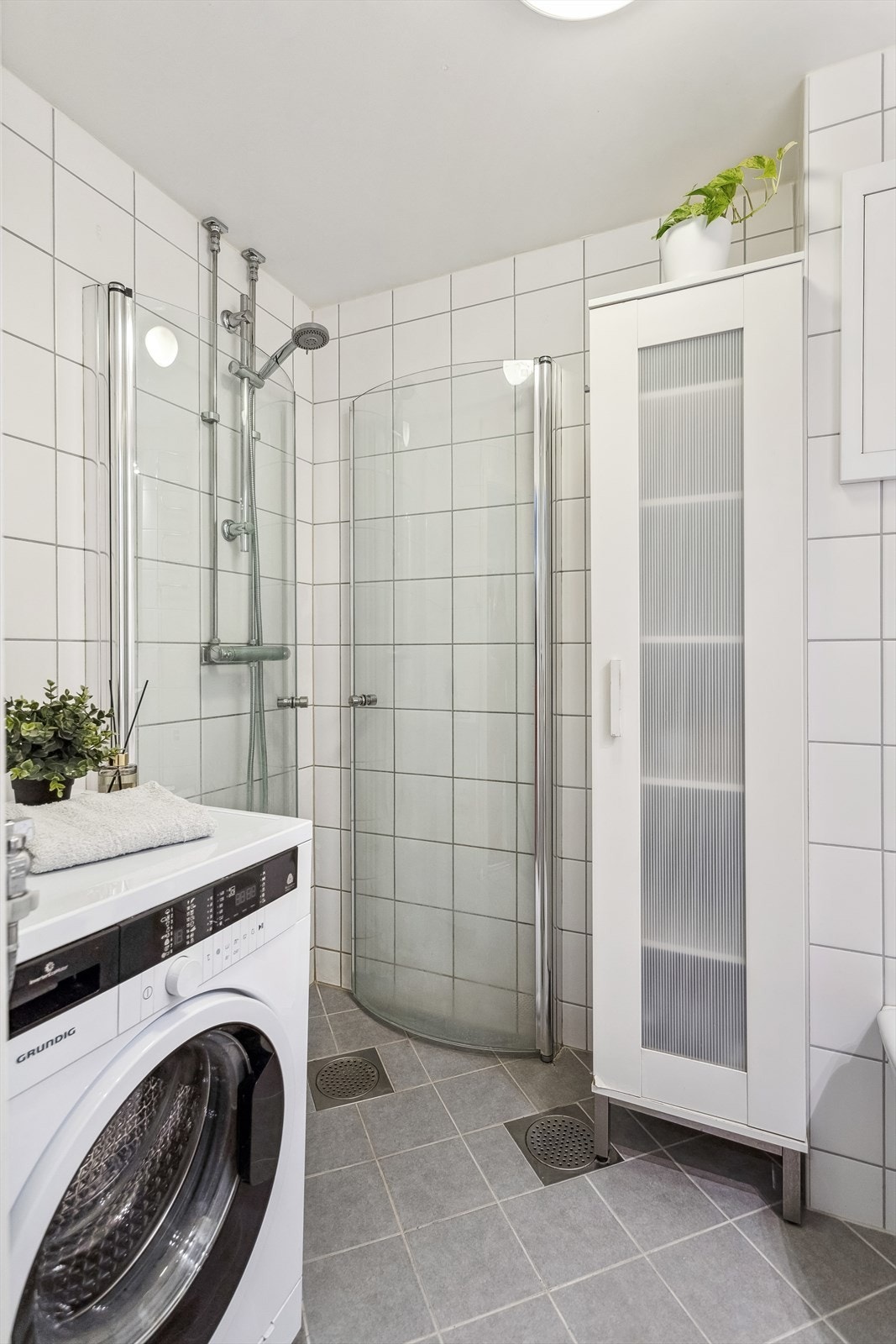 Badet er utstyrt med vegghengt toalett, dusjhjørne med glassvegger, innredning med servant og speil, samt veggskap Galleribilde
