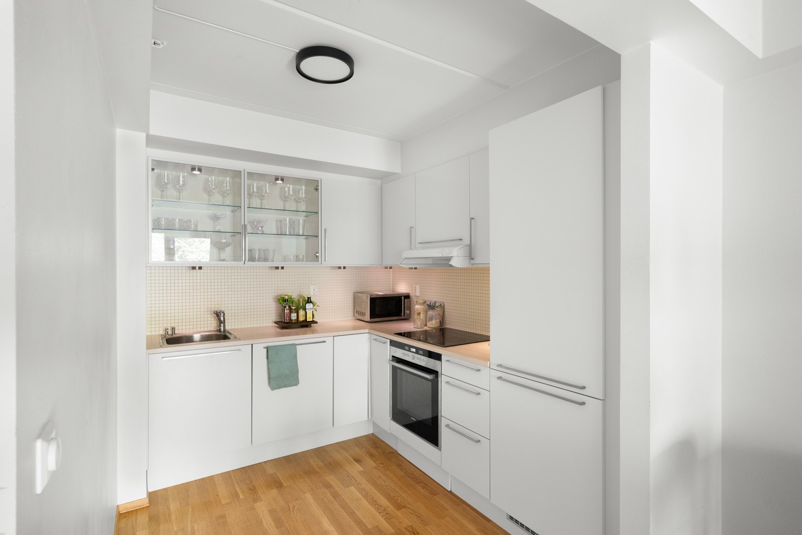 Lys kjøkkeninnredning fra HTH med glatte fronter og integrerte hvitevarer som komfyr, induksjon platetopp, oppvaskmaskin og kjøl-/fryseskap. Galleribilde