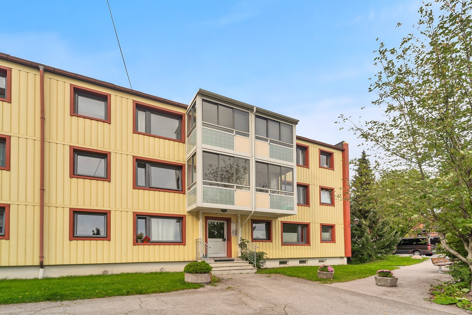 Fasade og inngangsparti til oppgangen. Nærområdet er opparbeidet med gressplen, busker og trær. Galleribilde