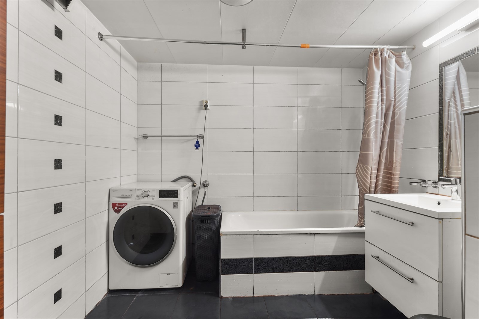 Baderomsinnredning bestående av benkeskap og høyskap med glatte fronter. Dusj i badekar, servant veggfestet klosett med innebygget sisterne og opplegg for vaskemaskin. Galleribilde