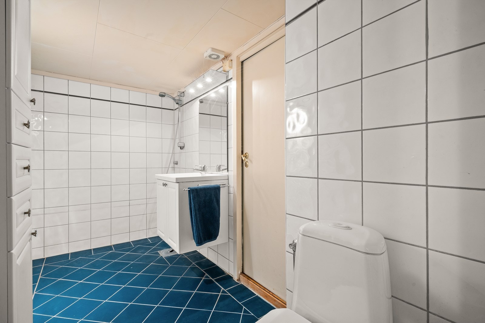 Badet inneholder toalett, helstøpt servant, skap under servant med profilerte fronter (skaper på siden) og dusjgarnityr. Galleribilde