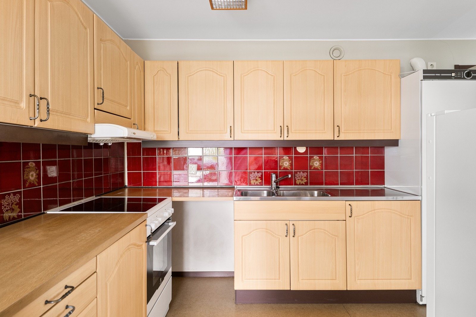 Eldre kjøkkeninnredning med profilerte fronter, laminat benkeplate, ventilator med kullfilter, fliser over benk og oppvaskkum. Galleribilde