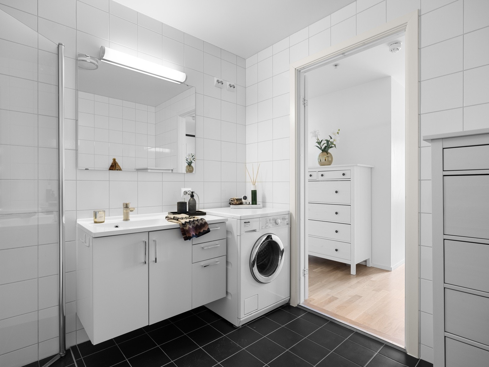 Rommet er innredet med vegghengt toalett, dusjhjørne med foldbare glassvegger, stort speil med belysning over og hvit vegghengt baderomsmøbel med vask og god oppbevaringsmulighet under med både skuffer og skap. Galleribilde