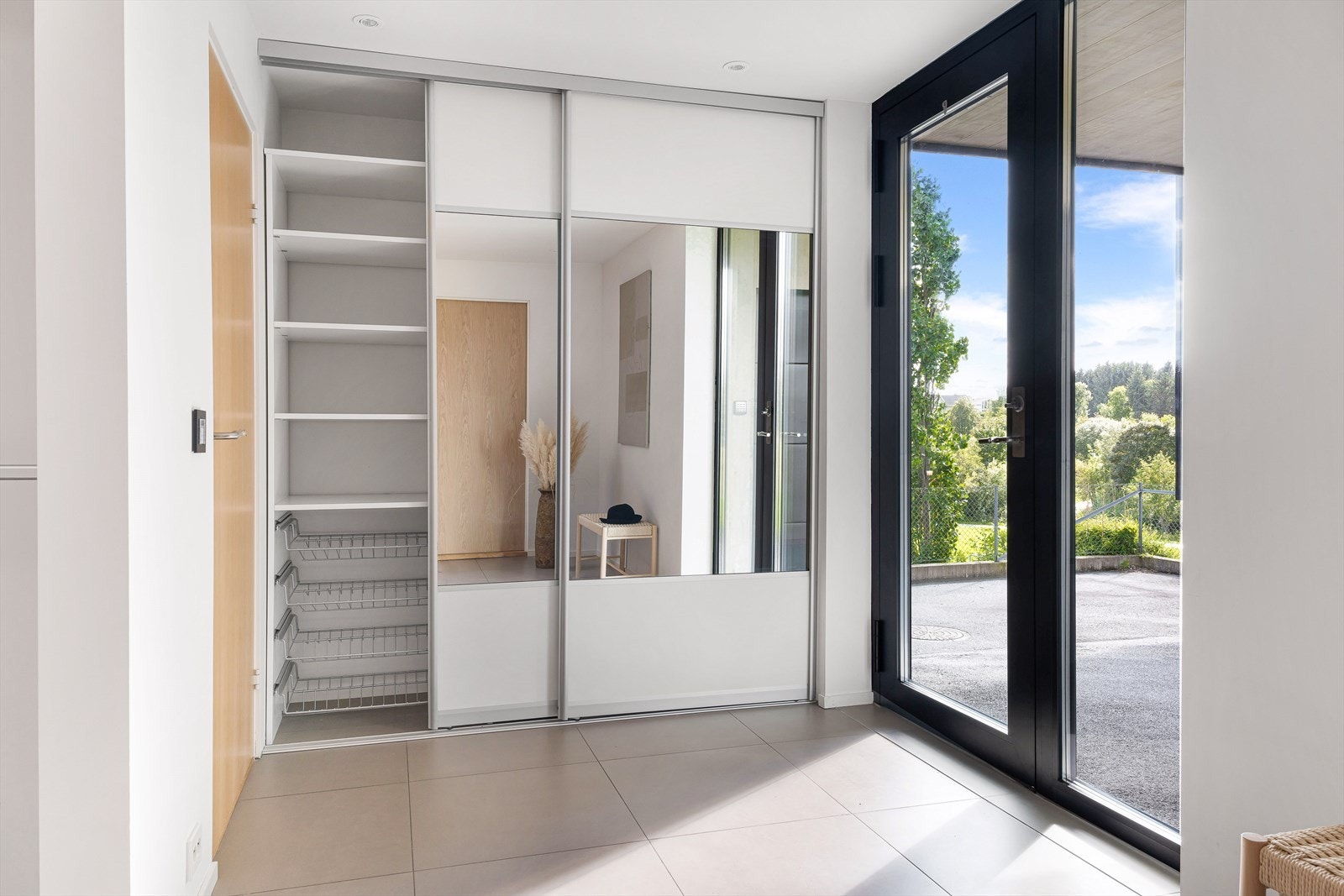 Inngangen til boligen er både funksjonell og estetisk tiltalende. Elegant glassdør som slipper naturlig lys inn i gangen, og integrert skyvedørsgarderoben gir god oppbevaringsplass for yttertøy og sko Galleribilde