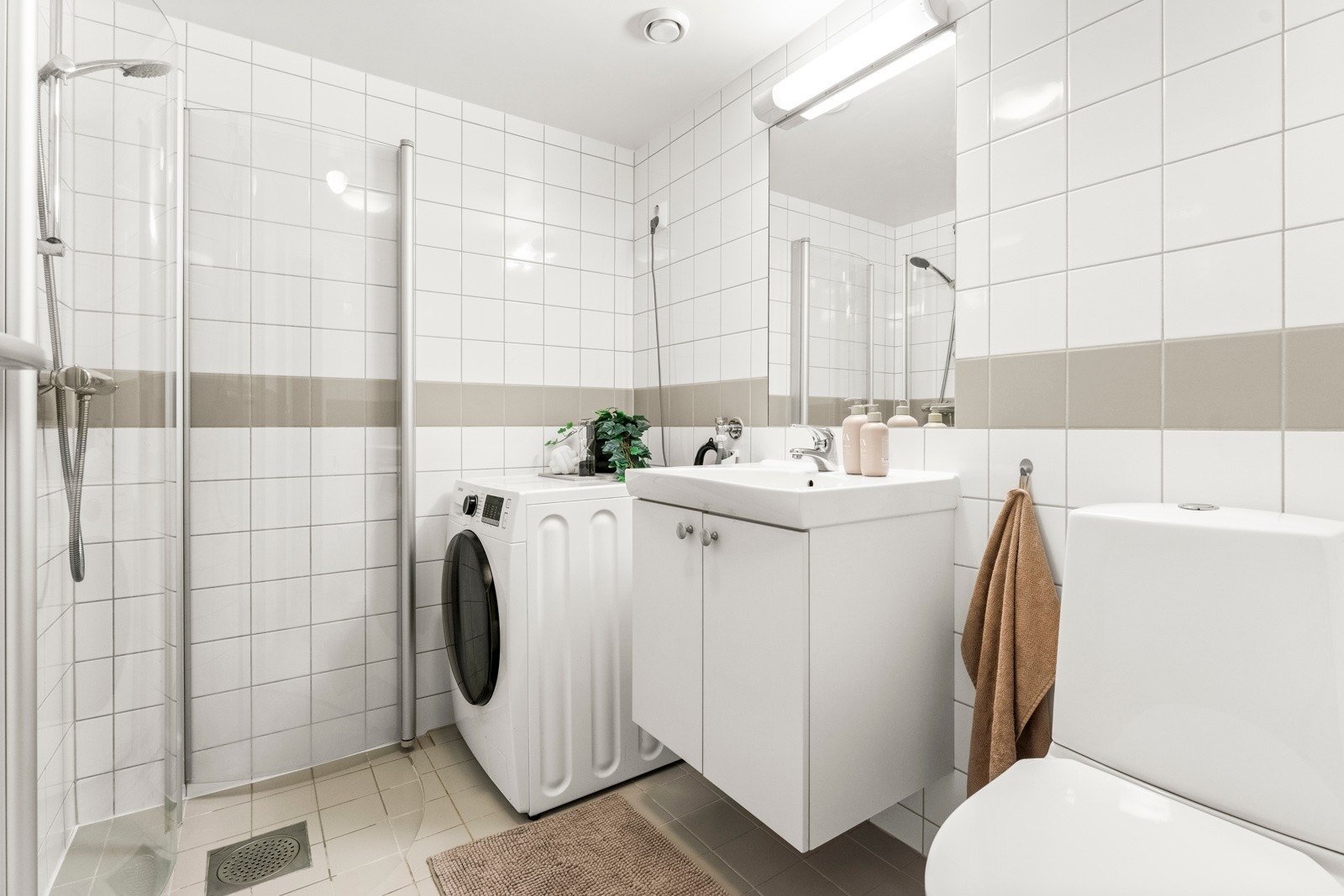 Flislagt baderom med behagelig gulvvarme og opplegg for vaskemaskin. Dusj med innfellbare dører i herdet glass og gulvstående toalett. Galleribilde