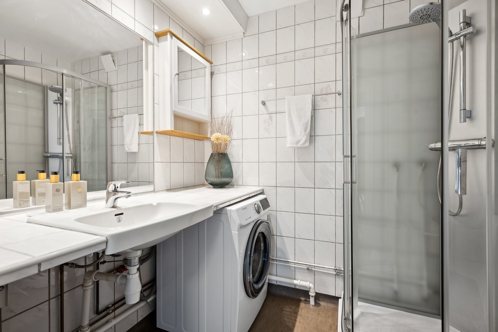 Bad fra byggeår, innredet med flislagt benkeplate, servant med ett-greps blandebatteri, innmurt speil, speilskap, vegghyller, gulvstående toalett og
dusjkabinett. Det er opplegg for vaskemaskin. Galleribilde