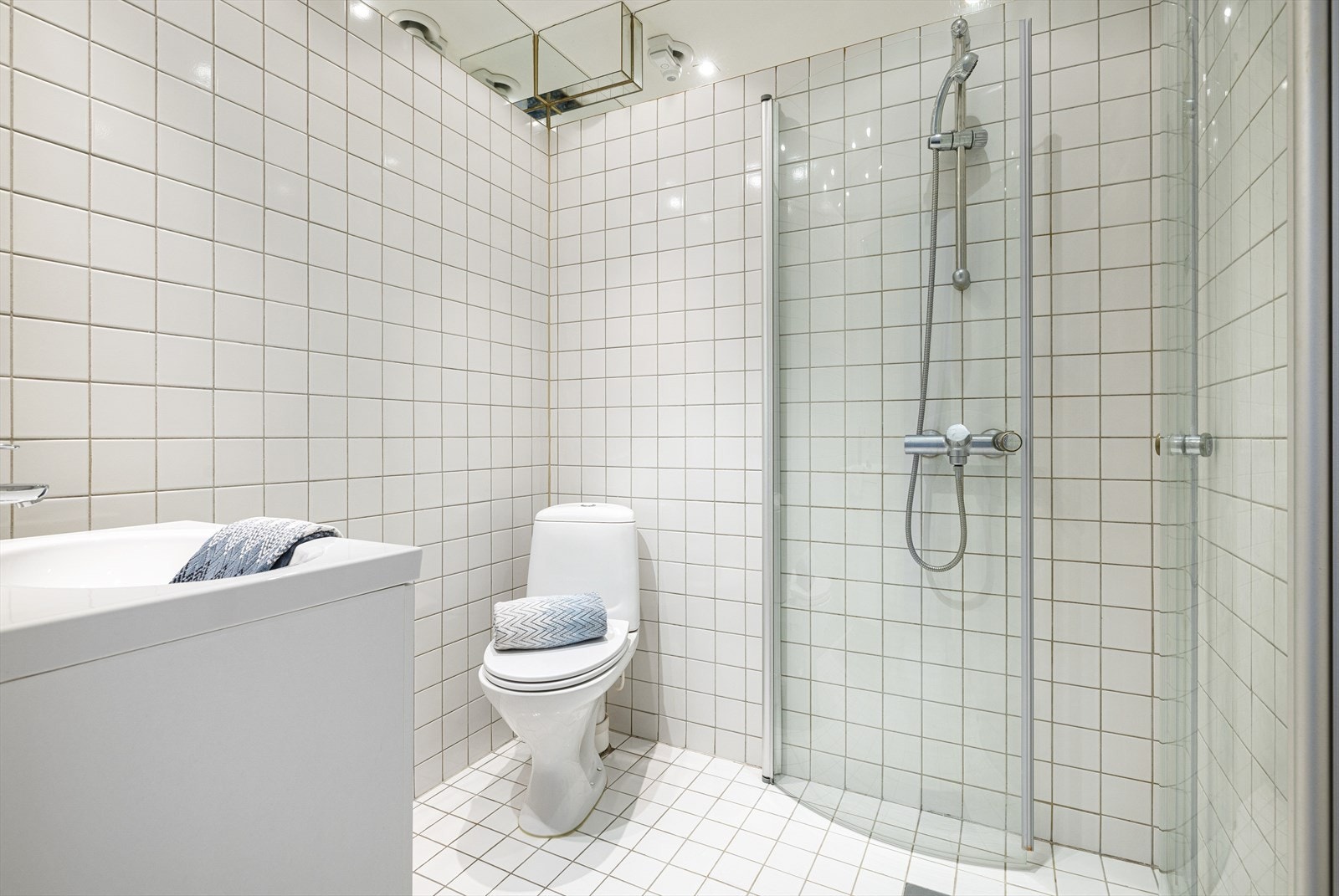 Innredningen består videre av servantskap med glatte, foliere fronter og heldekkende servant, innfliset speil på vegg over servant, gulvmontert klosett med utvendig sisterne, dusjhjørne med buede svingdører, sluk og termostatstyrt blandebatteri. Galleribilde