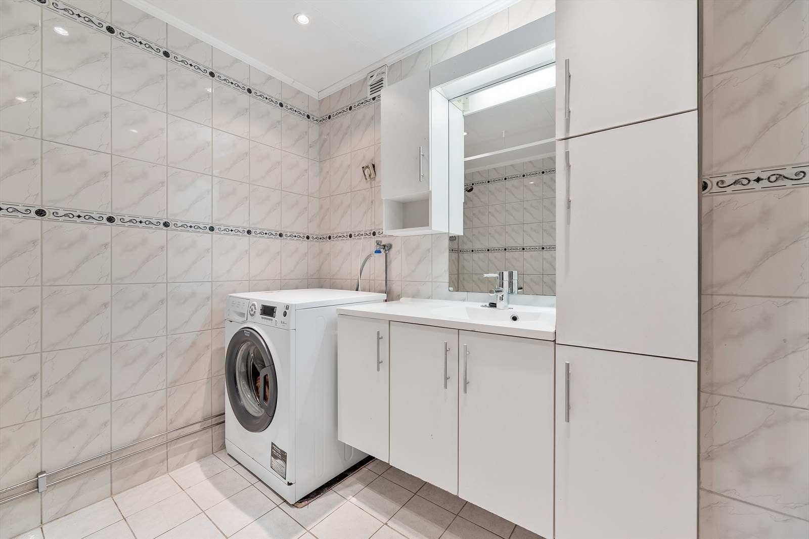 Badet er utstyrt med badekar med dusj, servantinnredning med under- og overskap samt opplegg og plass til både vaskemaskin og tørketrommel. Galleribilde