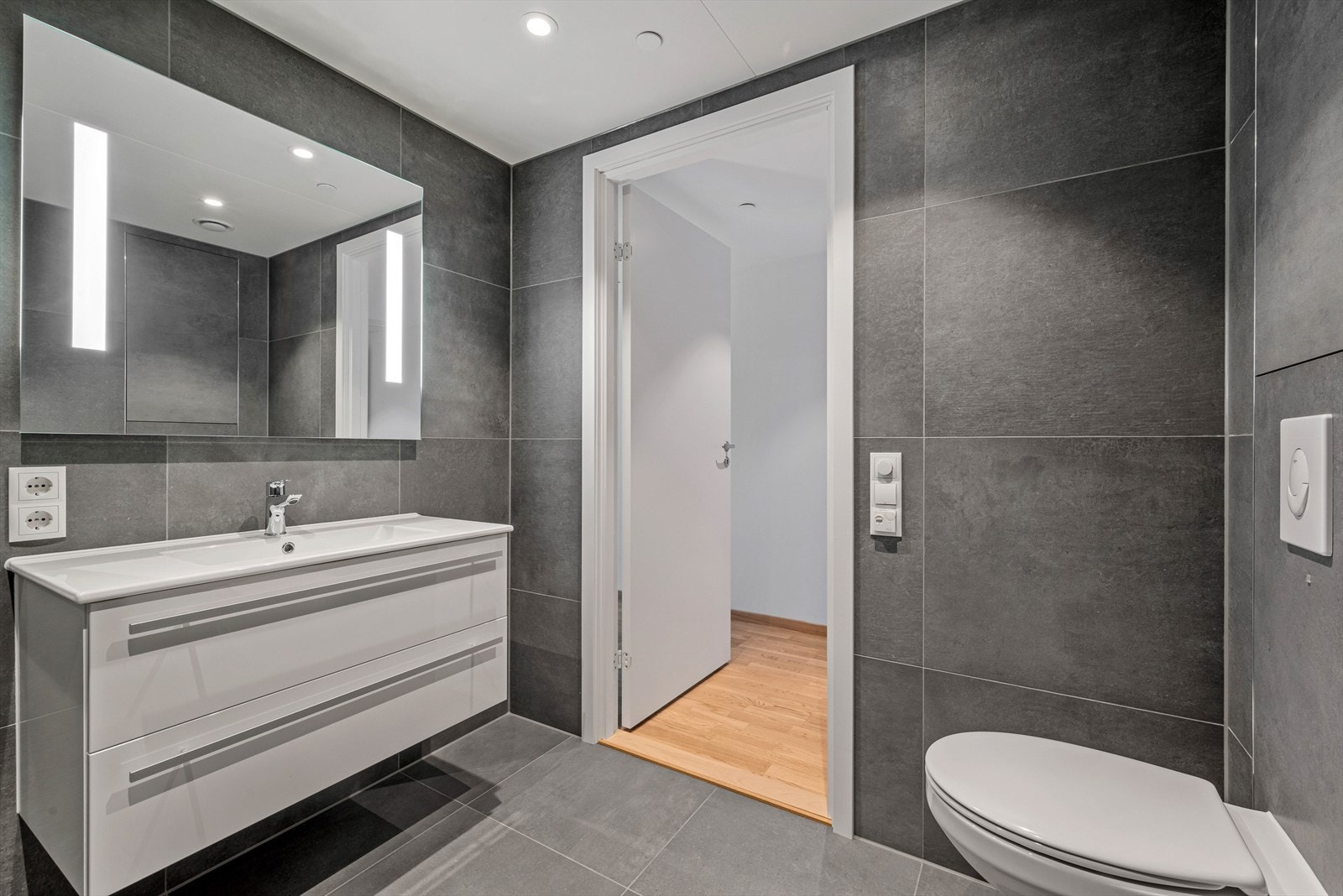 Badet måler ca. 4,5 kvm og har vegghengt speil med integrert belysning, innredning med skuffer og heldekkende servant. Galleribilde