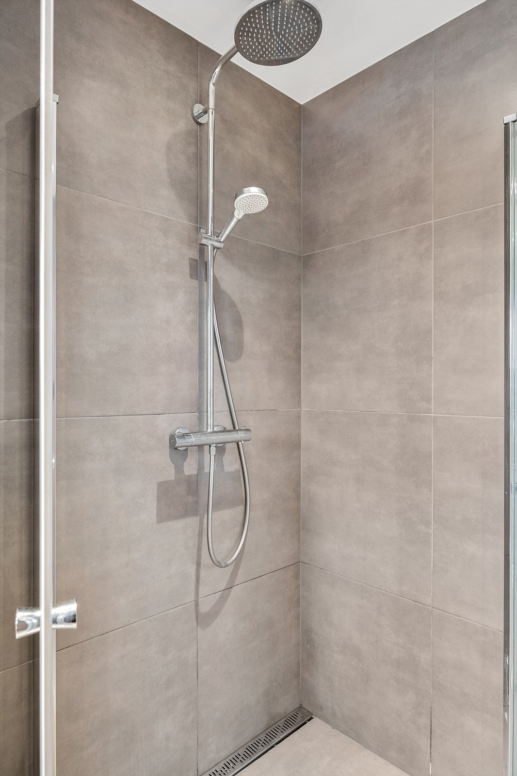 Badet er utstyrt med dusjhjørne med innfellbare glassvegger, vegghengt wc og servantinnredning med skuffer og overskap Galleribilde