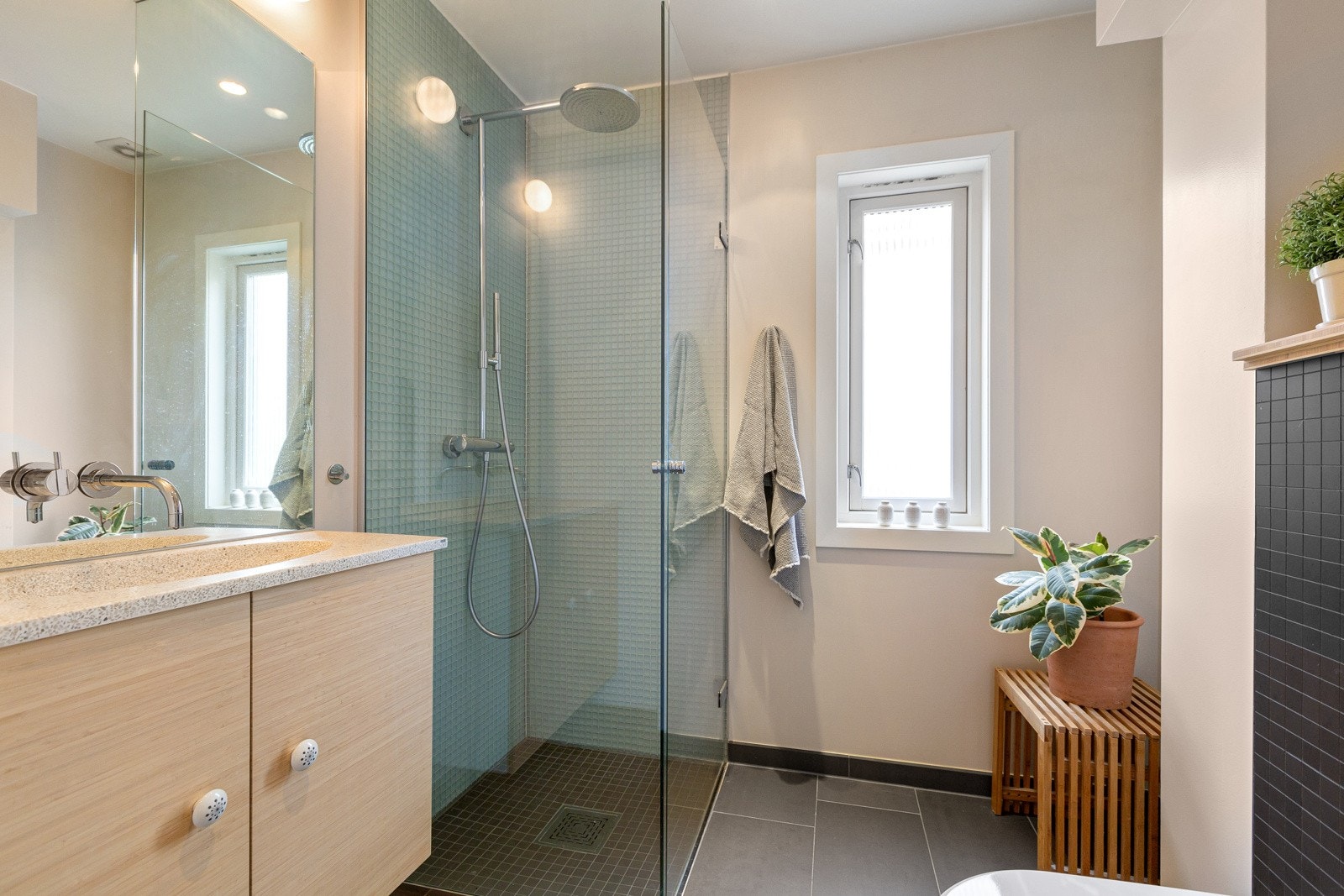 Innredning bestående av benkeskap med glatte fronter, servant i helstøpt plate, veggheng toalett og dusj med innfellbare dører i herdet glass. Galleribilde