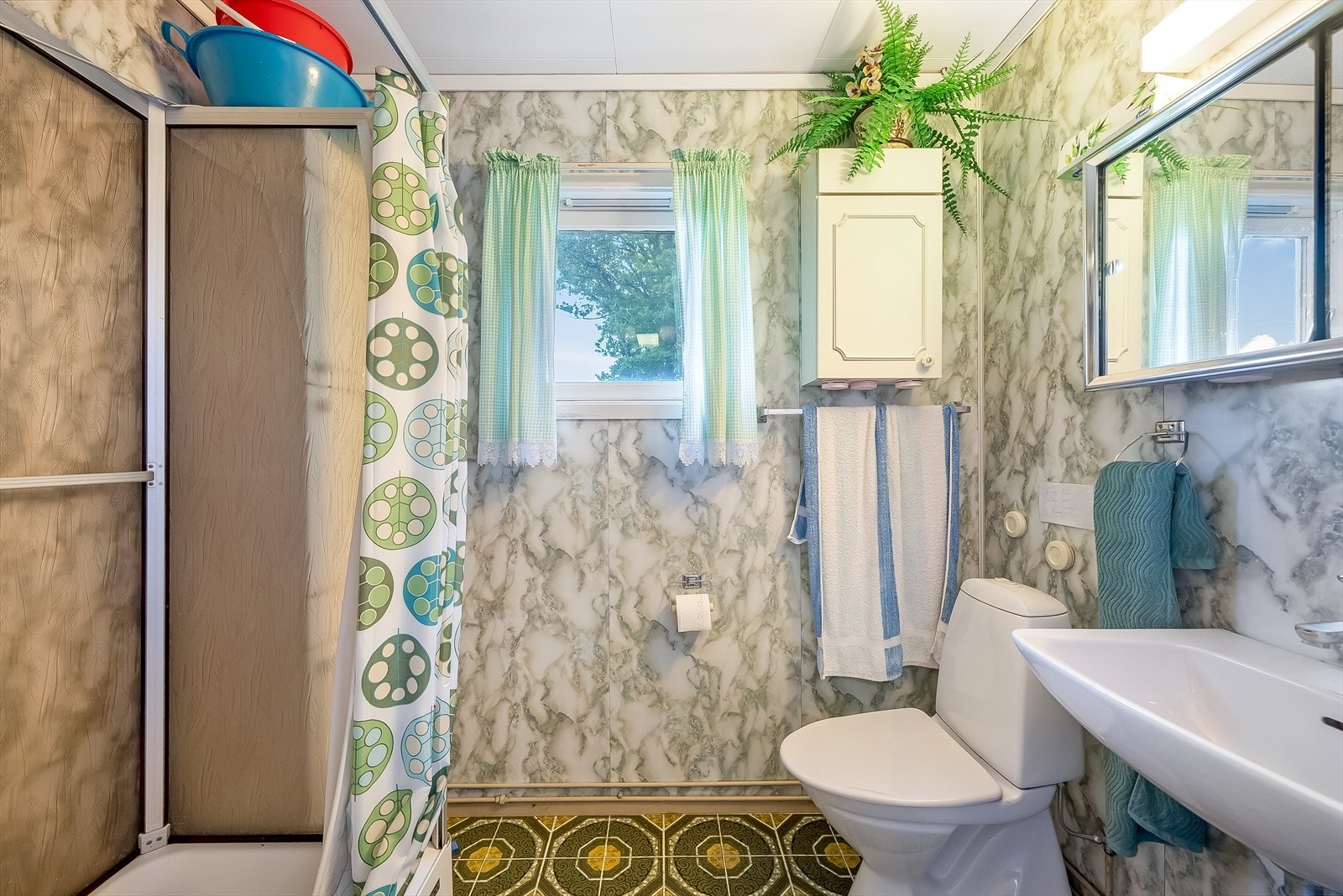 Eldre bad med inngang fra kjøkkenet med fliser på gulv og baderomsplater på vegg. Innredet med servant med speilskap, dusjkabinett og toalett. Galleribilde