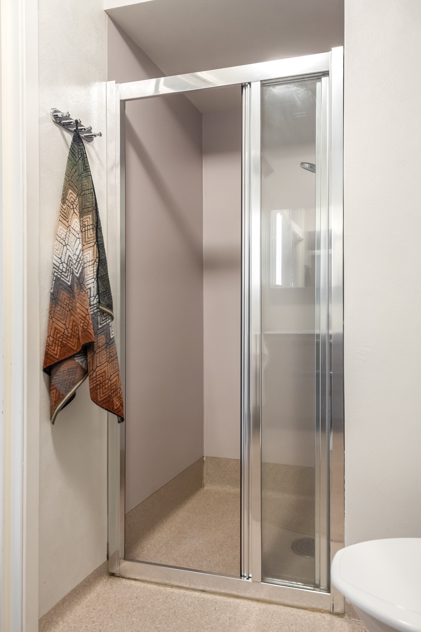 Badet består av dusjvegger av glass og dusjgarnityr på vegg, gulvmontert toalett, innredning med servant, opplegg for vaskemaskin (Kran og Galleribilde