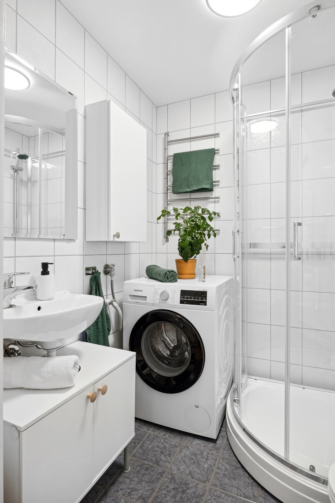 Lyst flislagt baderom som innehar dusjkabinett, servant m/servantskap, toalett, vegghengt skap og opplegg for vaskemaskin. Galleribilde
