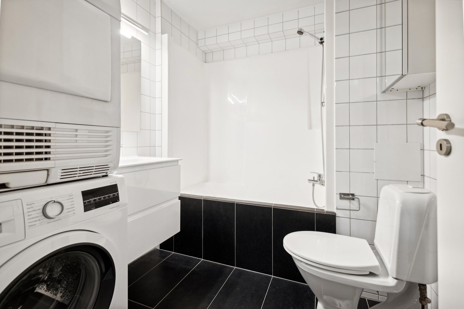 Badet er innredet med en baderomsinnredning med heldekkende servant, speil med overliggende lys, toalett og badekar med dusj. Galleribilde