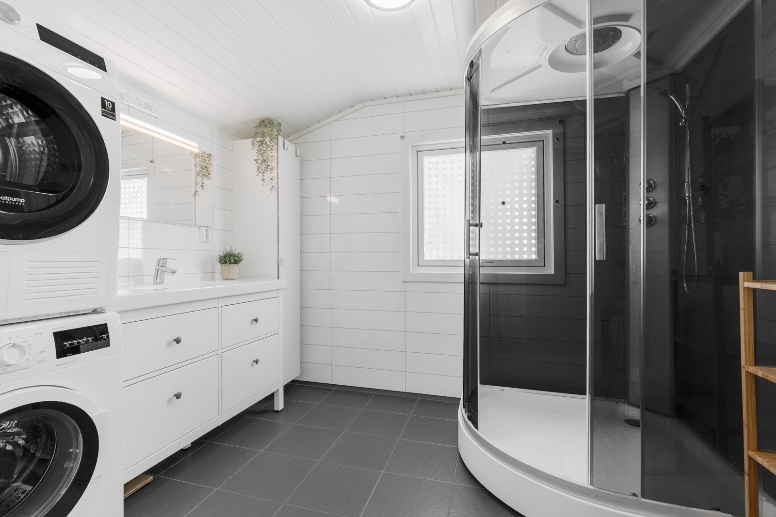 Delikat baderom bestående av servant med underskuffer, dusjkabinett, gulvstående toalett og opplegg til vaskemaskin Galleribilde