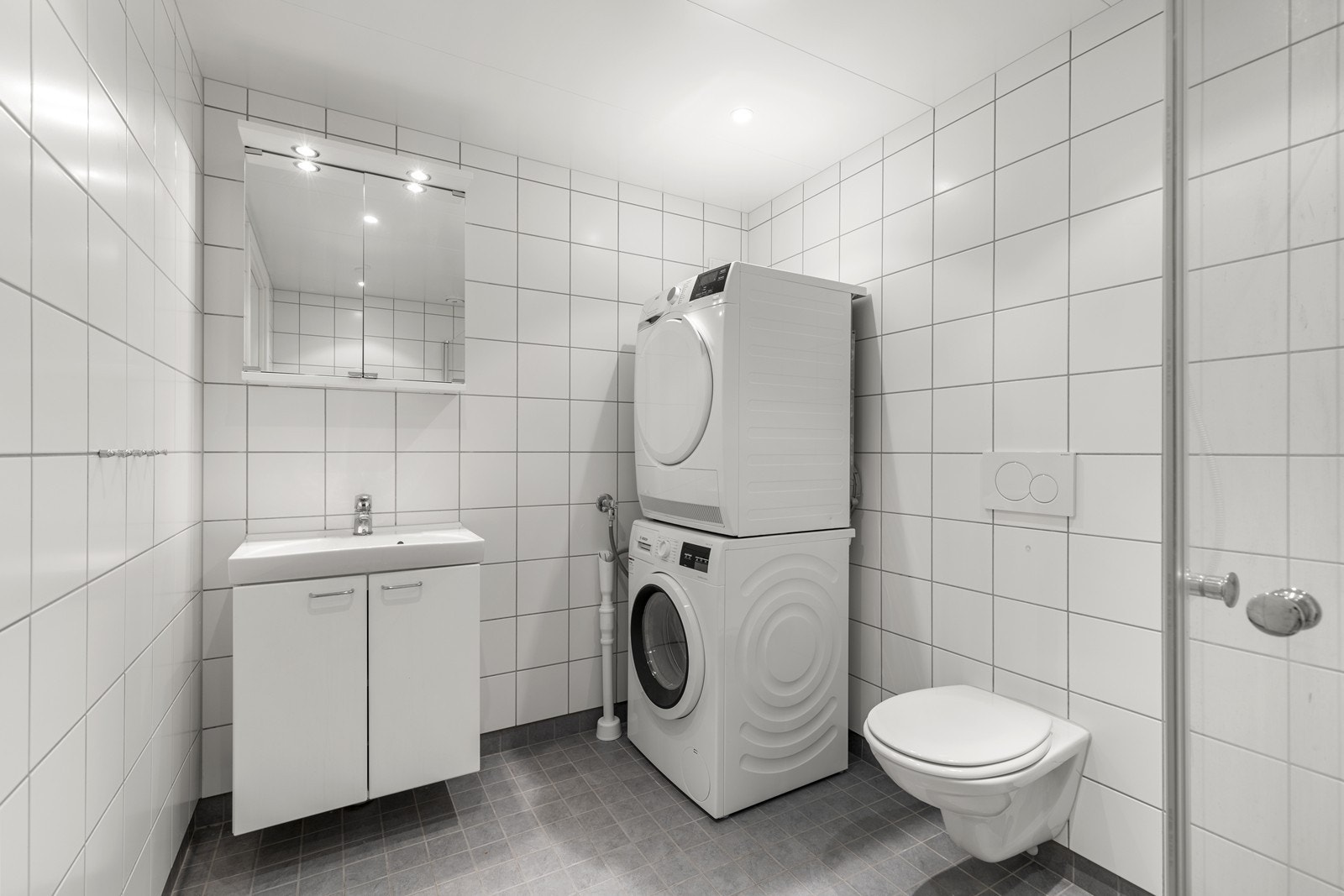 Leiligheten har et lyst og fint bad. Innredning med nedfelt servant, veggmontert toalett, dusjvegger/hjørne og opplegg for vaskemaskin. Galleribilde